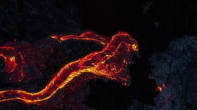 Aerial view of glowing molten lava flowing through dark volcanic rock at Kilauea in Hawaii County, Hawaii, United States.