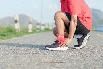 Naklejka premium Young adult man suffering from acute ankle pain during running workout. male runner holding his leg due to sports injuries, ankle sprains or achilles tendonitis. Medical and healthcare concept
