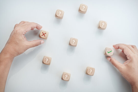 Professional hands choosing between incorrect and correct options on wooden cubes surrounded by question marks, representing decision making, problem solving, uncertainty, evaluation, choice, strategy