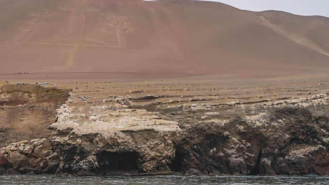 A gigantic ancient Inca geoglyph Candelabra of the Andes on the slope of a sandy hill. The famous trident pattern on the island. In the foreground &mdash; an eroded coastline, the ocean. Peru. Paracas 
 