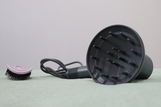 Gray Hair Dryer Diffuser Attachment With Cord Lying Beside Small Pink Cleaning Brush On Soft Pale Surface, Shown Against Minimal Light Background With Copy Space For Grooming, Beauty Care