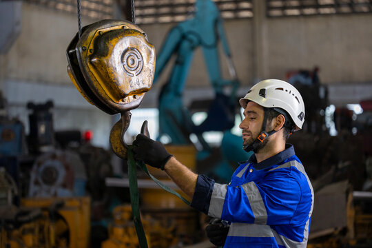 Caucasian engineer worker is using overhead crane hoist to carry raw materials inside metal sheet manufacturing factory for heavy industry