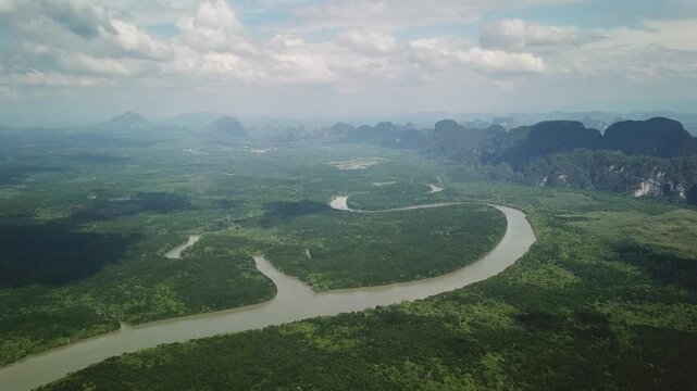 Aerial view of the winding river flowing through lush mangrove forests and limestone karst mountains in Phang Nga, Thailand.