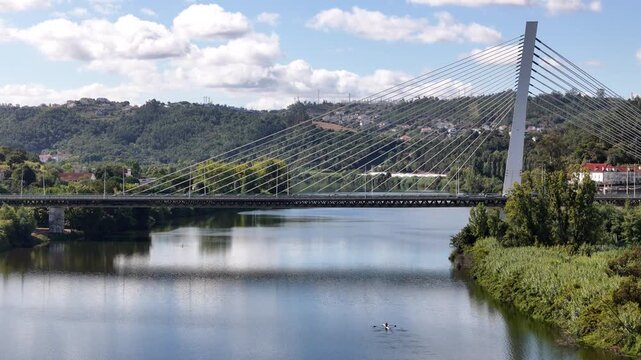 Aerial view of the cable-stayed Ponte Rainha Santa Isabel crossing the Mondego River with lush green banks and a small boat on the water in Coimbra, Coimbra, Portugal.