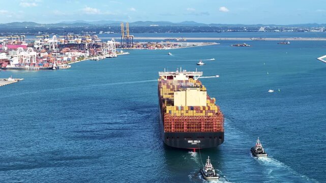 container ship fully loaded with cargo escorted by tugboats navigating through a blue sea towards a bustling commercial port terminal. Global maritime logistics and international trade transport conce