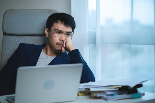 Stressed Businessman Working on Laptop While Using Smartphone at Office Desk, Managing Business Communication Under Pressure. 