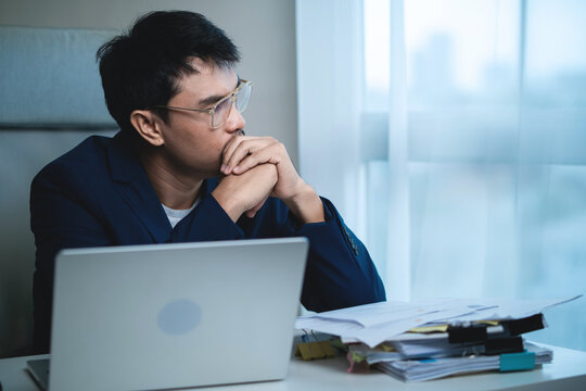 Stressed Businessman Sitting at Office Desk and Holding His Head While Working on Laptop, Showing Workplace Pressure and Frustration