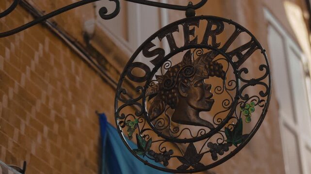 Metal street sign with Bacchus silhouette and grape details hanging outside authentic Italian restaurant osteria.