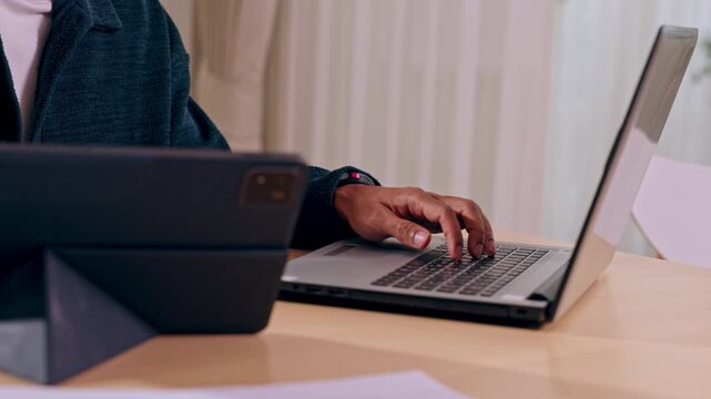 Remote work professional typing laptop beside tablet home office desk, focused hands and posture during online communication, soft natural light, modern technology workspace, productive digital