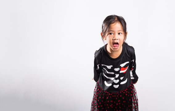 Halloween kid costume celebration featuring young person wearing skeleton dress while making funny face expression in studio against bright white background surface