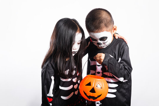 Halloween celebration features happy kid and young friend wearing skeleton costume holding orange pumpkin bucket while smiling brightly together during holiday festival against white background