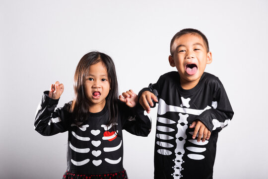 Halloween celebration featuring smiling young kid duo wearing spooky skeleton costumes while playing playfully against white background for autumn holiday party fun