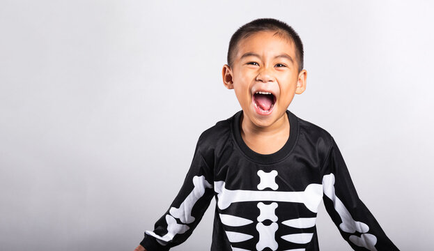 Halloween kid wearing skeleton costume shouting happily while celebrating spooky holiday festival on clean white isolated background for seasonal party concept