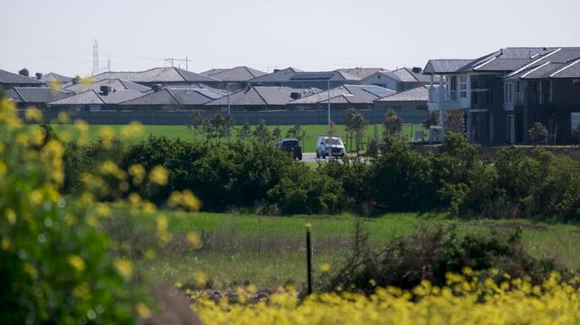 New suburban housing estates and vehicles driving along a neighborhood street behind vacant land in Truganina, Melbourne, Australia. Interface between undeveloped land and new residential estate