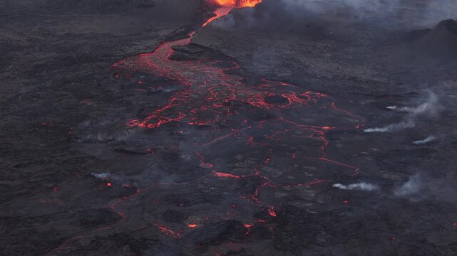 Aerial view of glowing red lava flowing through dark volcanic terrain with rising smoke in Reykjavik, Reykjavikurborg, Iceland.