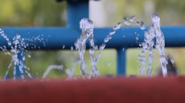 An image showing a layer of water emerging from a hole in a pipe and dripping down drop by drop.