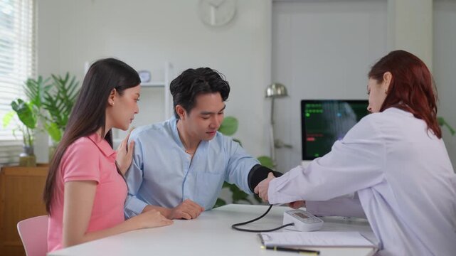 Female doctor measuring blood pressure of a male patient with his wife supporting him during a medical consultation