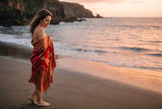 Young woman in red sarong standing on beach at sunset