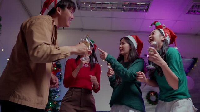 Young Asian friends wearing Santa hats dancing and drinking champagne together. Happy people celebrating Christmas and New Year's Eve at a party