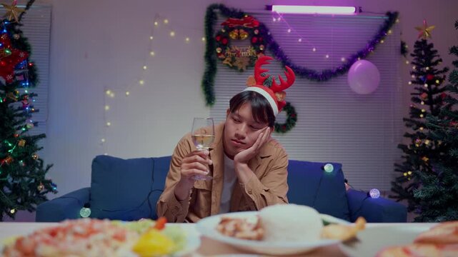 Lonely asian man feeling sad and bored celebrating Christmas alone at home with a glass of champagne