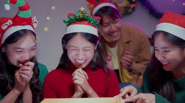 Asian woman showing ecstatic surprise while opening a magic christmas gift box with glowing light surrounded by friends