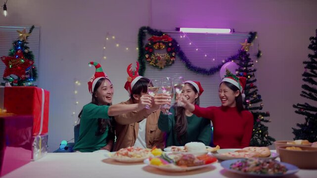 Cheerful Asian friends enjoying dinner party, toasting with wine glasses and celebrating Christmas or New Year's eve at home