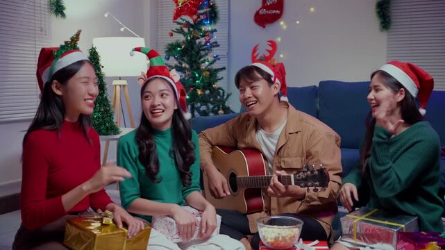 Group of asian friends singing christmas songs and playing guitar during a party at home on Christmas eve
