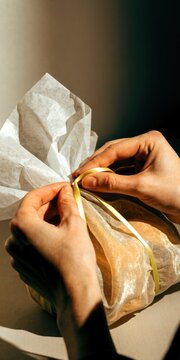 Economy creator concept. Hands tying a string around a wrapped gift or package with textured paper in warm lighting.