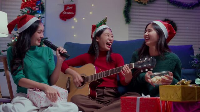 Joyful asian friends singing karaoke and playing guitar during a Christmas party at home in the living room