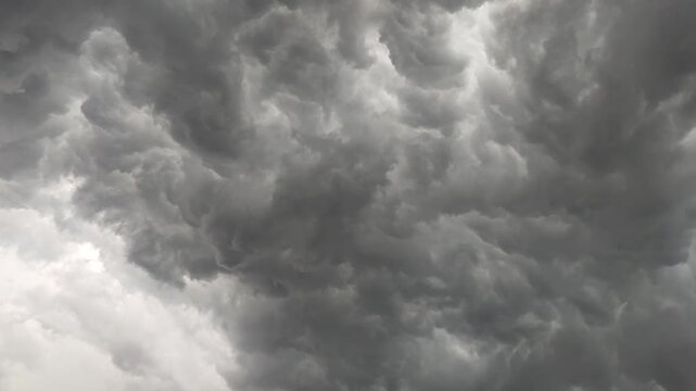 A dramatic and powerful display of nature unfolds as dark, heavy mammatus clouds gather across the sky, signaling an intense and foreboding weather event