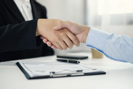 Business partners shaking hands over contract document after successful negotiation at office desk for partnership agreement concept