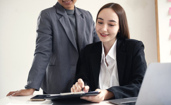 Two Asian businesswomen analyzing financial charts report and working together on laptop for business strategy planning and teamwork concept