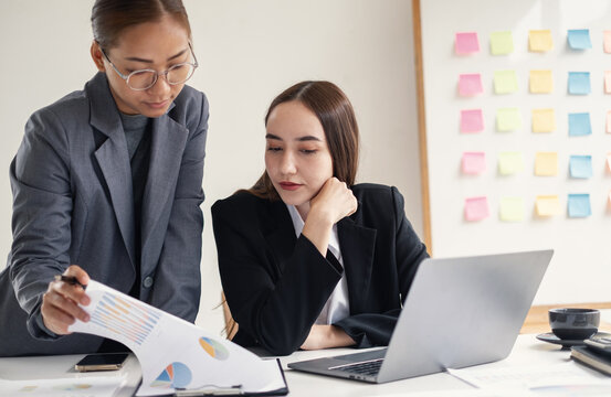 Two Asian businesswomen analyzing financial charts report and working together on laptop for business strategy planning and teamwork concept