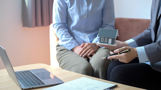 Real estate agent holding house model and pen consulting client for home loan mortgage agreement purchase and property insurance concept