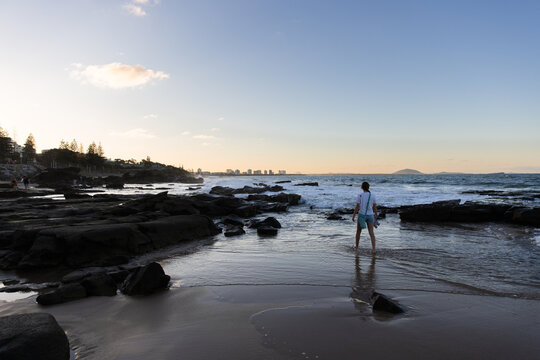 Young girl walking barefoot in the rocky shoreline at dusk