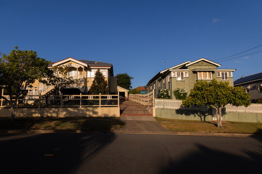 Streetscape featuring two elevated Queensland-style homes bathed in late afternoon sunlight