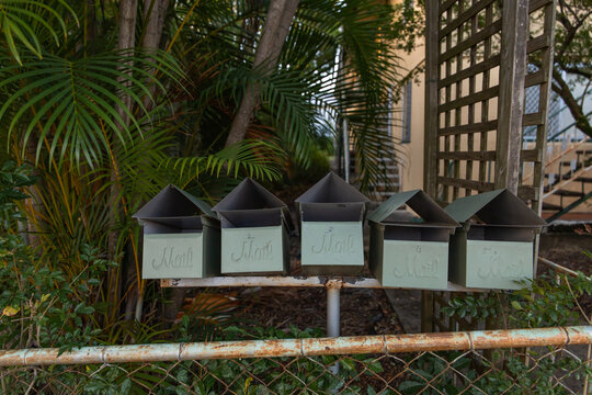 five old letter boxes in front of a unit block on a rusty fence