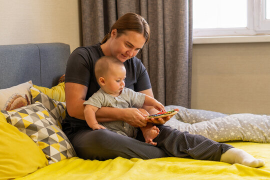 Woman Helping Baby Explore Wooden Gear Toy On Bed