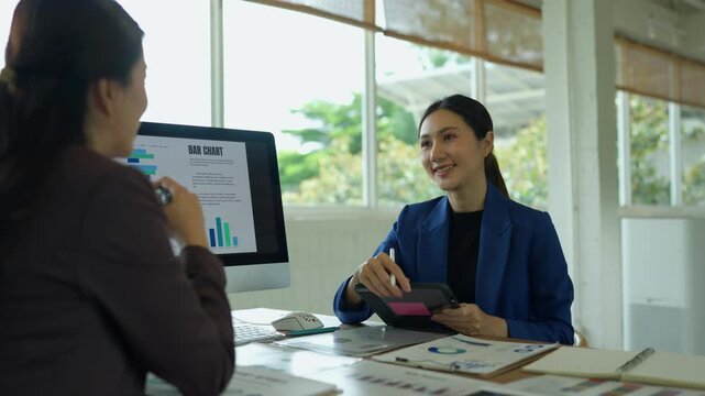 Asian businesswomen discussing financial data and bar chart analysis during a corporate meeting in a modern office environment