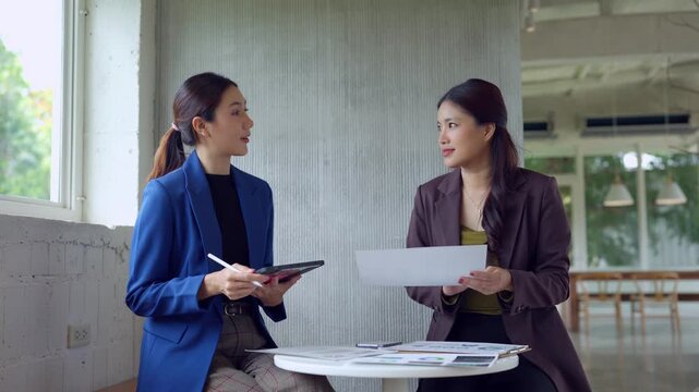 Two young asian businesswomen discussing strategy and project plans during a business meeting in a modern office