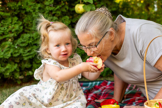 Smiling Granddaughter Sharing Bitten Apple With Grandmother Outdoors