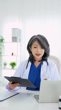 Confident asian doctor talking on video call by looking at camera from hospital with patients. concept of online counseling, medical advice and consultation.