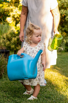 Toddler Carrying Large Watering Can Beside Grandmother in Garden