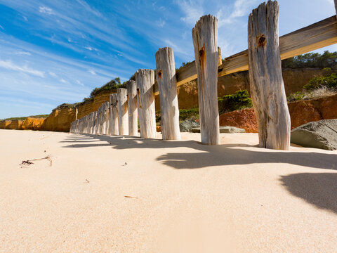 Weathered timber groyne stretching across sandy beach beneath blue coastal sky