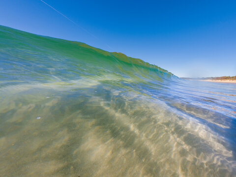 Crystal clear ocean wave rolling toward sandy beach beneath blue sky