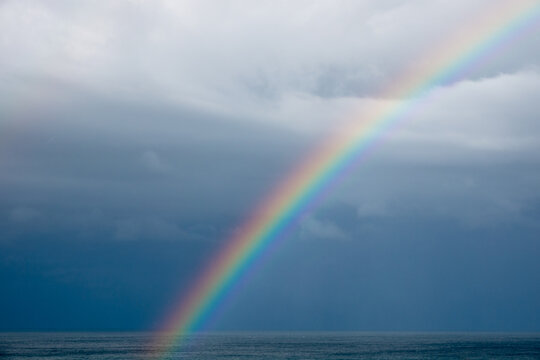 Brilliant rainbow stretching across stormy ocean beneath dramatic cloudy sky