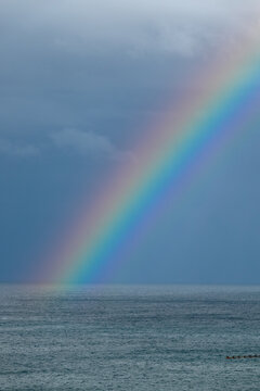 Vibrant rainbow arching across calm ocean beneath dramatic storm clouds
