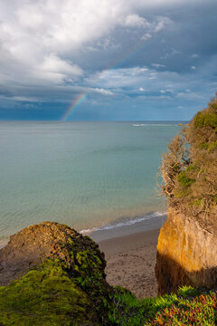 Rainbow stretching across calm ocean beside rugged coastal cliffs at sunset