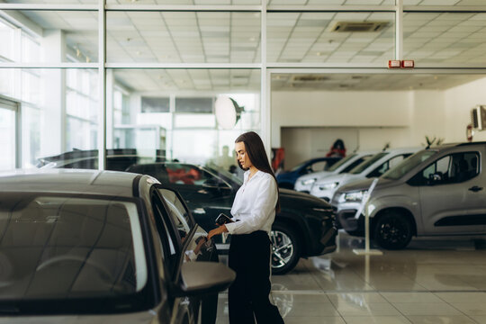 Woman checking new automobile in dealership showroom
