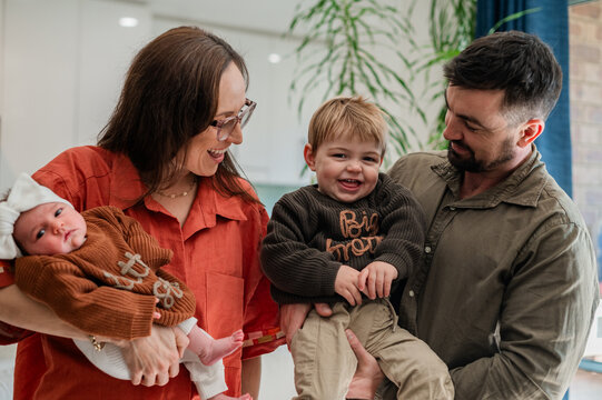 Parents hold their children in a kitchen, smiling and engaging with each other in a family moment